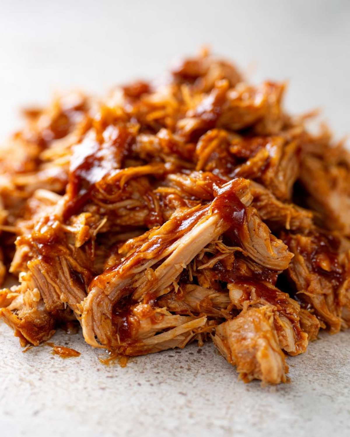 A close-up, macro shot of shredded, tender slow cooker pulled pork coated generously in barbecue sauce.