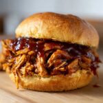 Close-up of a delicious sandwich overflowing with saucy slow cooker pulled pork on a toasted bun.