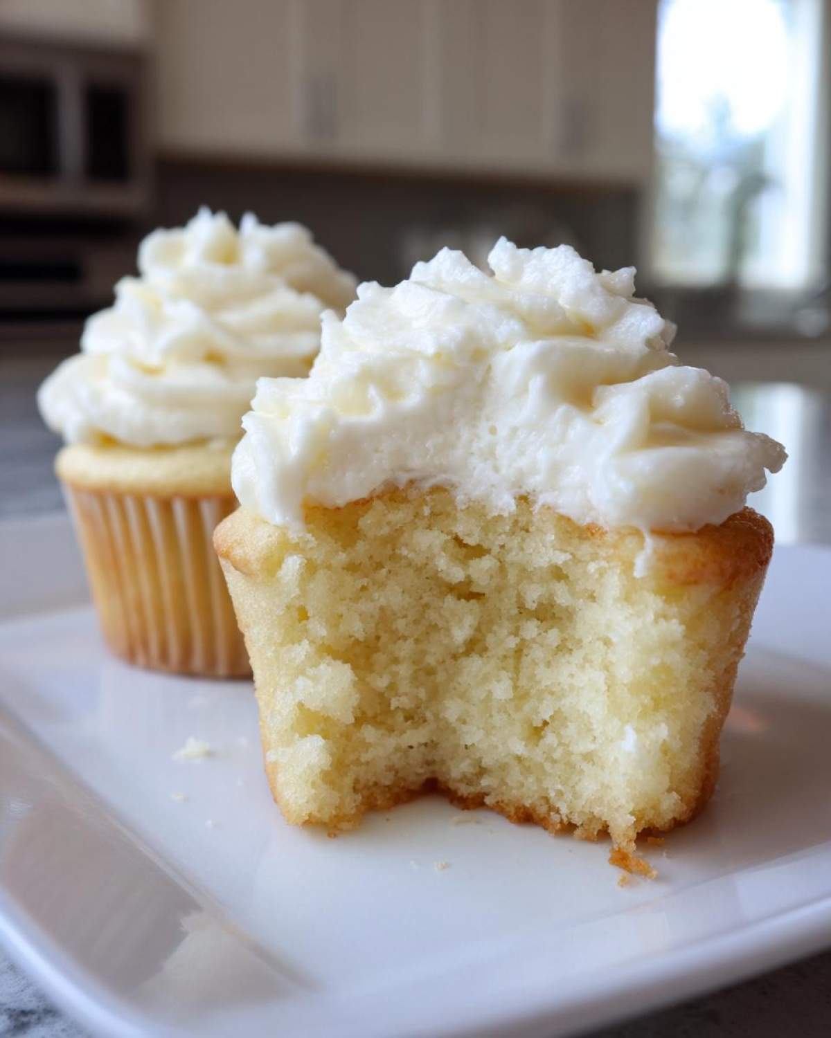 Close-up of a vanilla cupcake with a bite taken out, showing the moist crumb and thick white frosting.