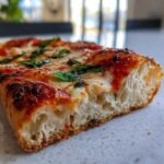 Close-up of a slice of pizza showing the airy crumb structure of the sourdough discard pizza dough base.