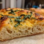 Close-up of the airy, open crumb structure of sourdough discard pizza dough topped with melted cheese and basil.