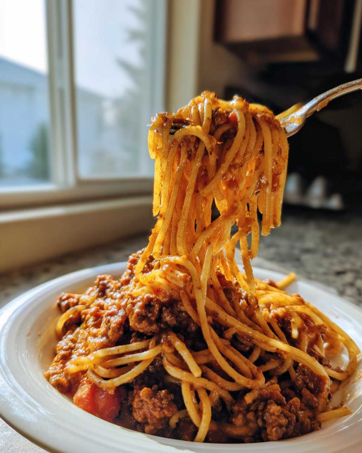 A fork lifting long strands of spaghetti coated in rich bolognese sauce from a white bowl.