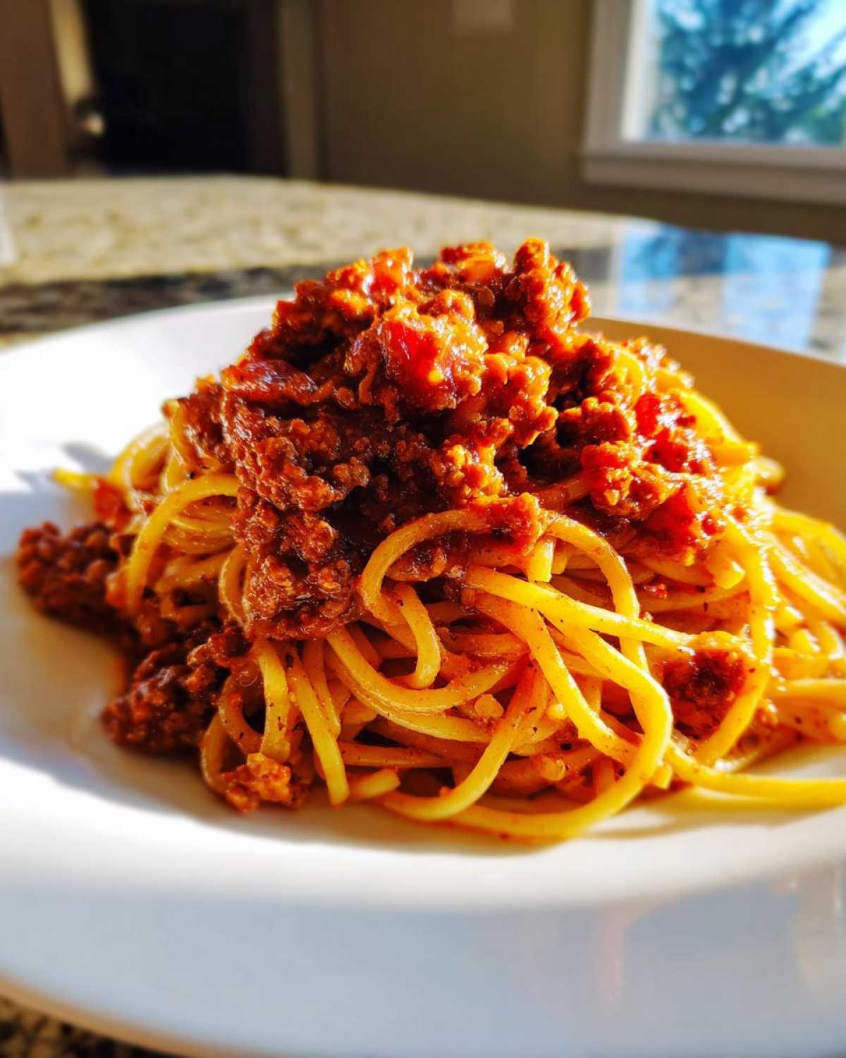 Close-up of spaghetti topped generously with rich, thick bolognese sauce served on a white plate.