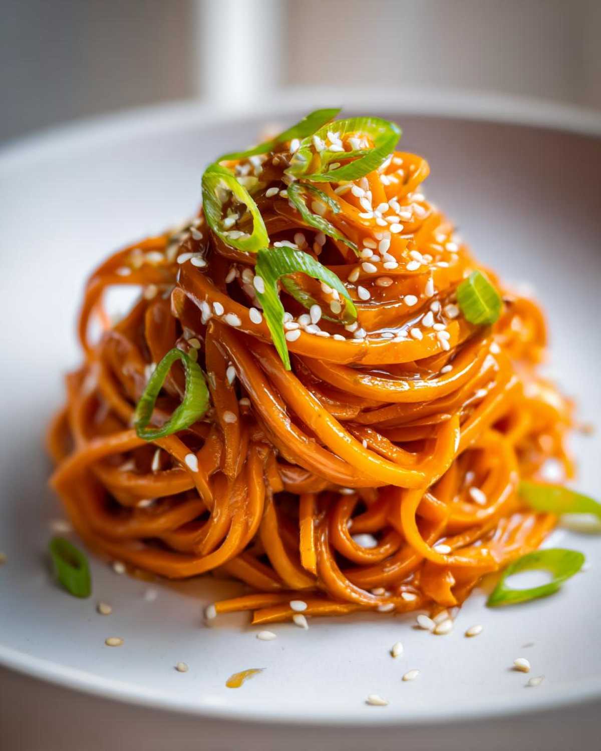 Close-up of spiralized raw carrot salad styled like noodles, topped with sesame seeds and green onions.