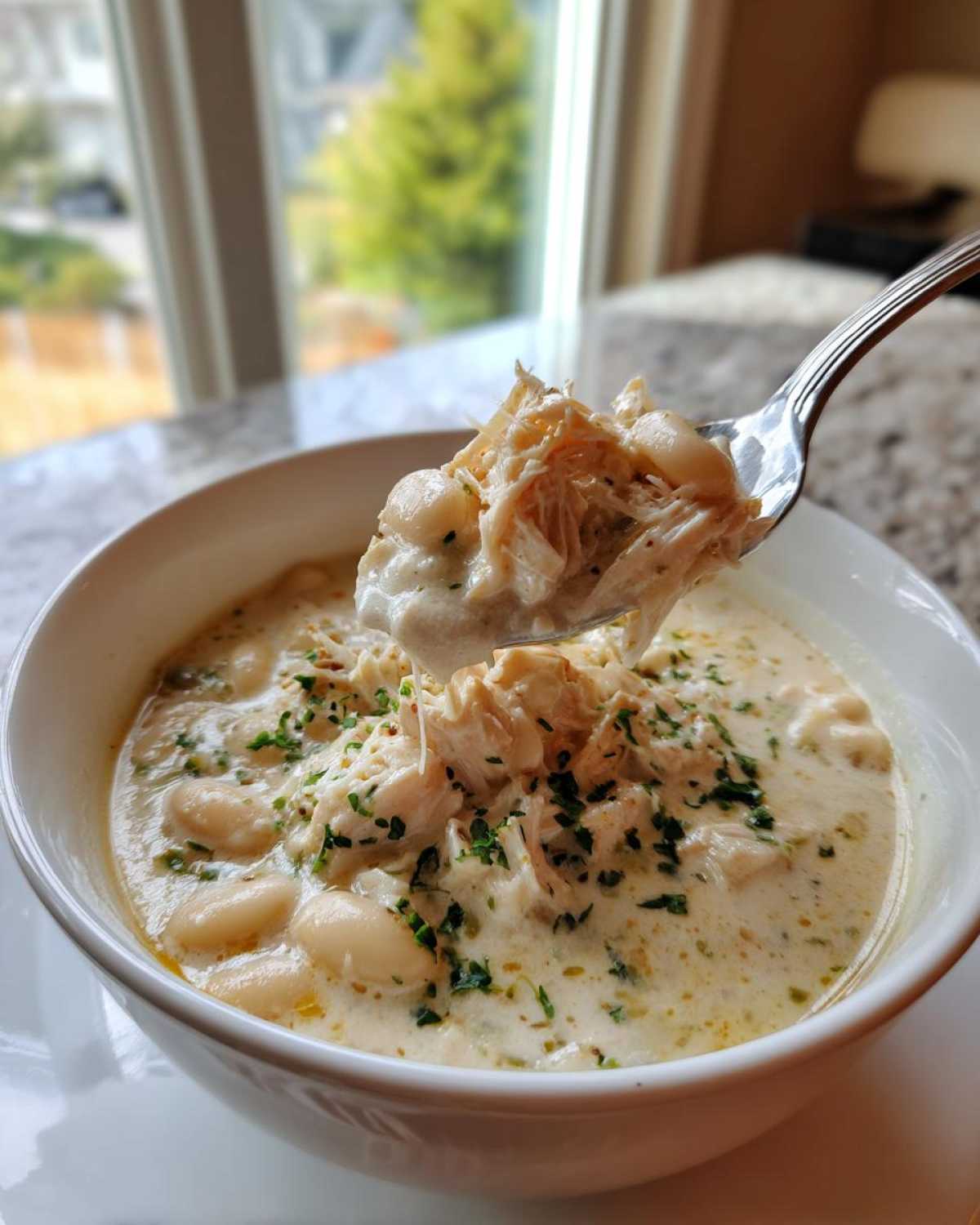 A spoonful of creamy crockpot white chicken chili, showing shredded chicken and white beans, lifted from a bowl.