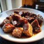 Close-up of tender, cubed crockpot steak bites coated in a rich, glossy brown sauce with visible garlic pieces.