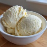 Three scoops of creamy, light yellow protein ice cream served in a small white bowl.