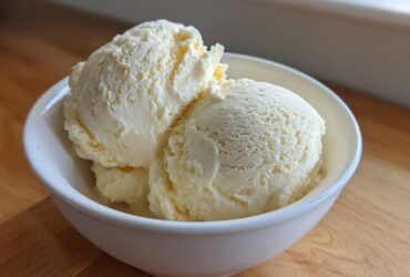 Three scoops of creamy, light yellow protein ice cream served in a small white bowl.