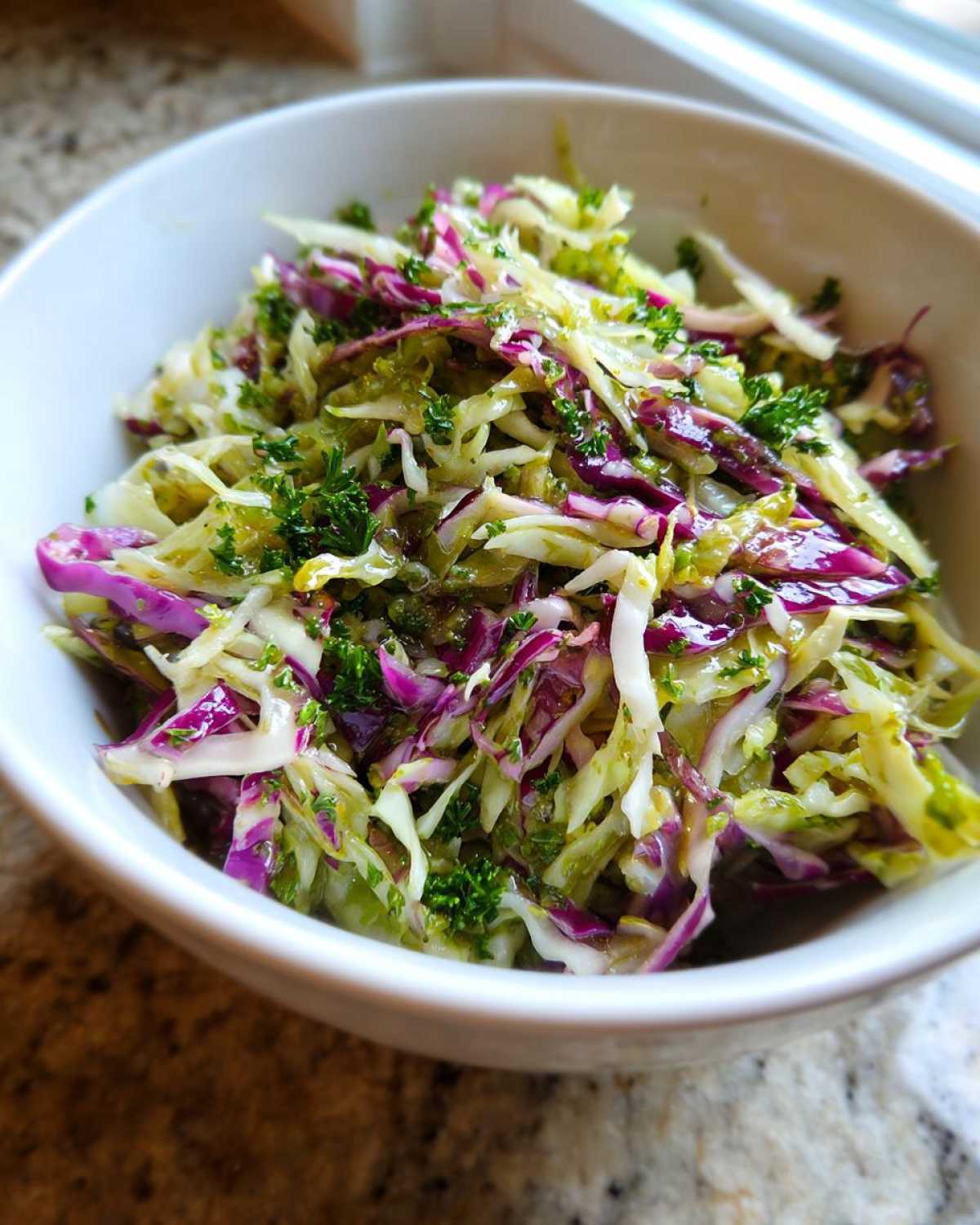 Close-up of a fresh, vibrant cabbage salad made with shredded red and green cabbage, topped with herbs and dressing.