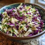 A close-up of a vibrant cabbage salad made with shredded red and green cabbage, topped with fresh parsley.