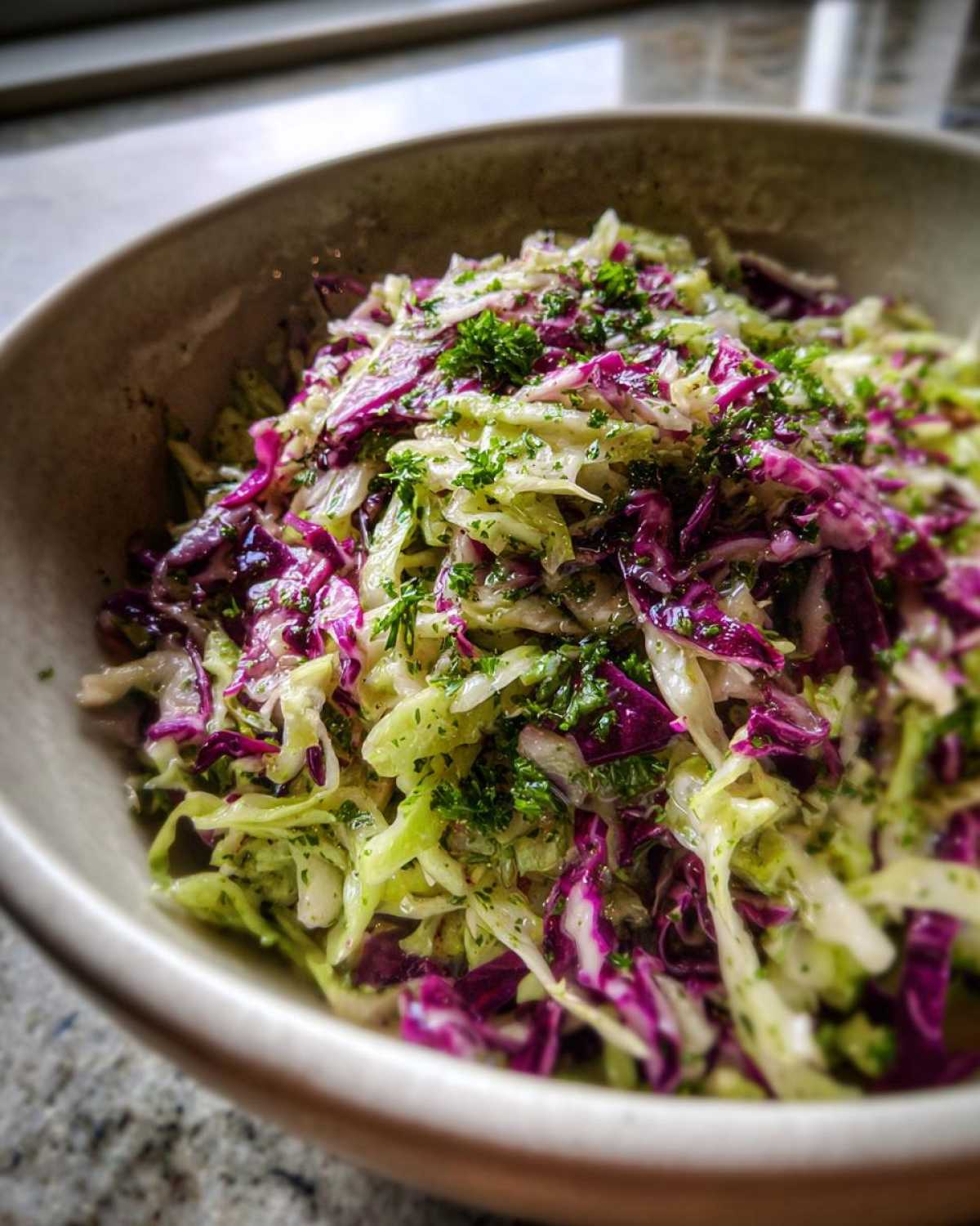 Close-up of a vibrant cabbage salad featuring shredded red and green cabbage tossed in dressing and topped with fresh parsley.