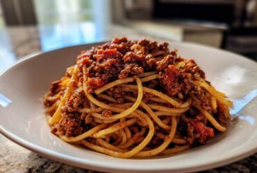 A close-up of spaghetti noodles generously topped with hearty bolognese sauce in a white bowl.