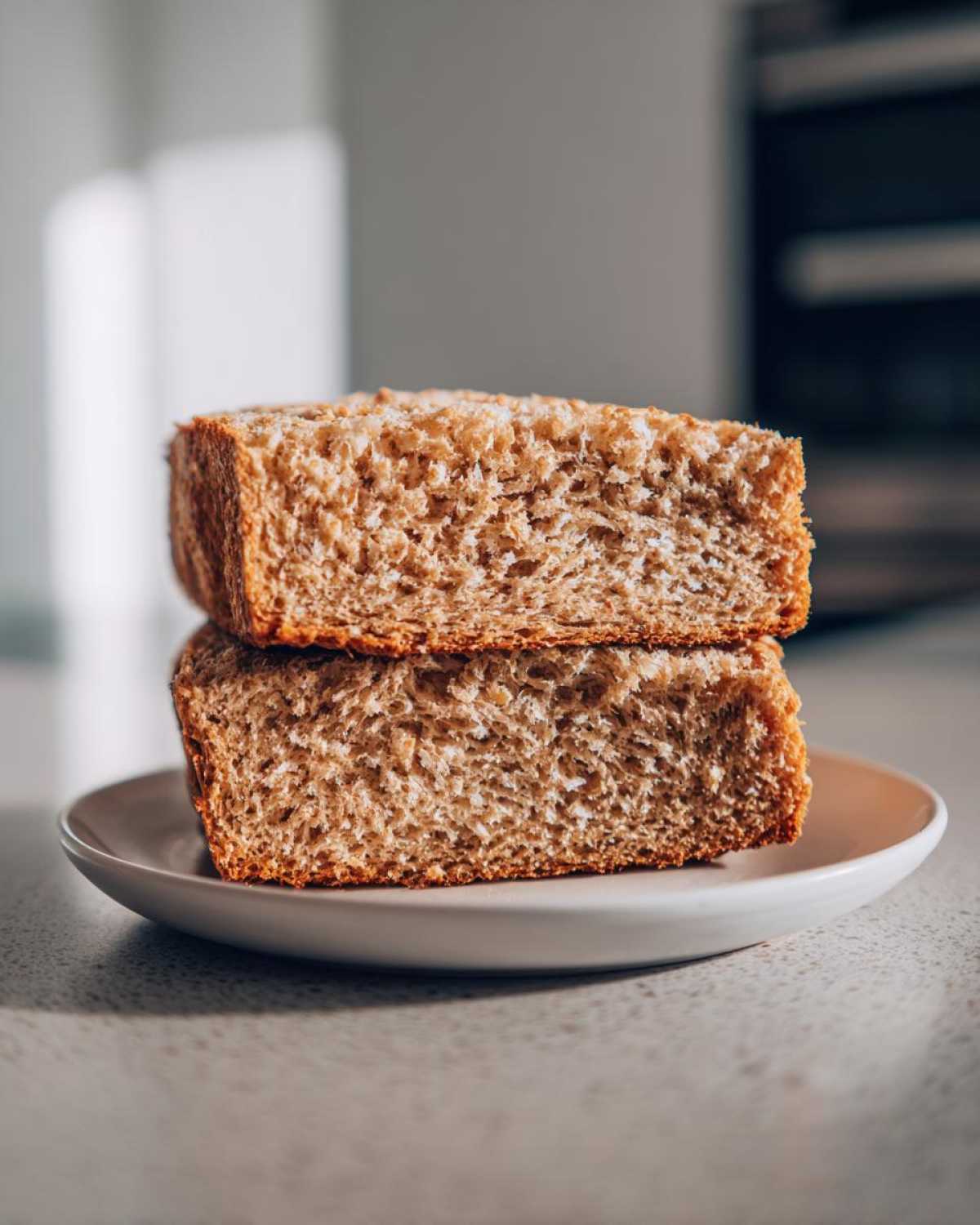 Two thick slices of homemade whole wheat bread stacked on a small plate, showing the soft, open crumb texture.