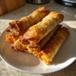 A stack of golden brown, crispy Air Fryer Crispy Buffalo Chicken Taquitos piled on a white plate.