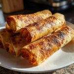A stack of golden brown, crispy Air Fryer Buffalo Chicken Taquitos served on a white plate.
