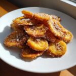 A pile of golden Air Fryer Crispy Cinnamon Sugar Banana Chips heavily coated in sugar crystals on a white plate.