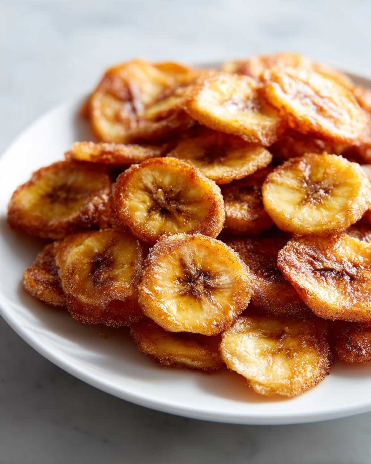 A pile of golden brown Air Fryer Crispy Cinnamon Sugar Banana Chips served on a white plate.