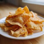 A pile of golden brown, crispy Air Fryer Crispy Tortilla Strips dusted heavily with cinnamon sugar on a white plate.