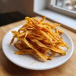 A close-up of a mound of golden, seasoned Air Fryer Crispy Tortilla Strips piled high on a small white plate.