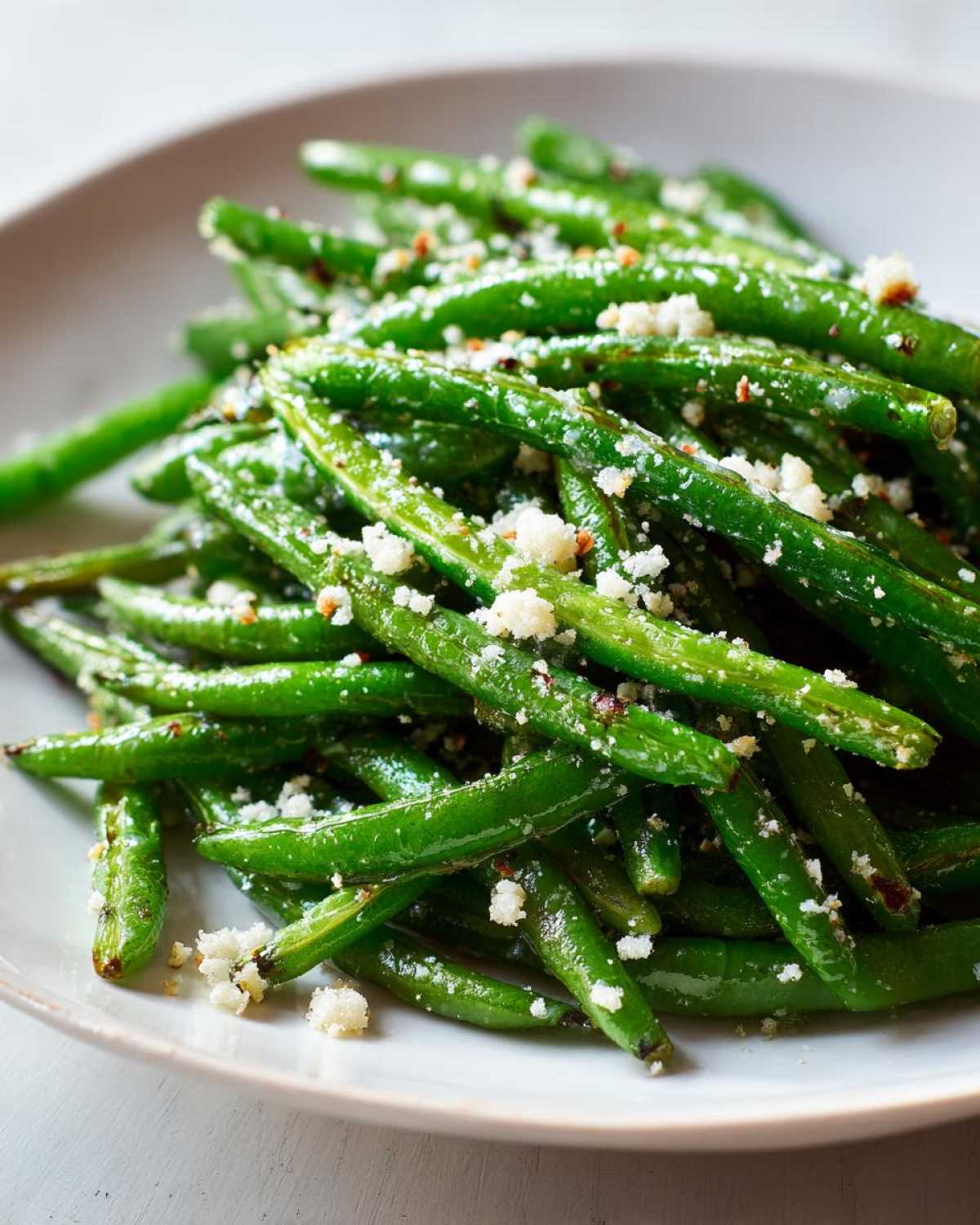 Close-up of vibrant green beans tossed with garlic and sprinkled with grated Parmesan cheese, ready to eat.