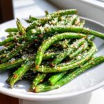 Close-up of crispy Air Fryer Garlic Parmesan Green Beans piled high on a white plate, topped with grated cheese.