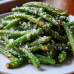 Close-up of crispy Air Fryer Garlic Parmesan Green Beans sprinkled with grated cheese on a white plate.