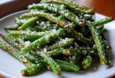 Close-up of crispy Air Fryer Garlic Parmesan Green Beans sprinkled with grated cheese on a white plate.