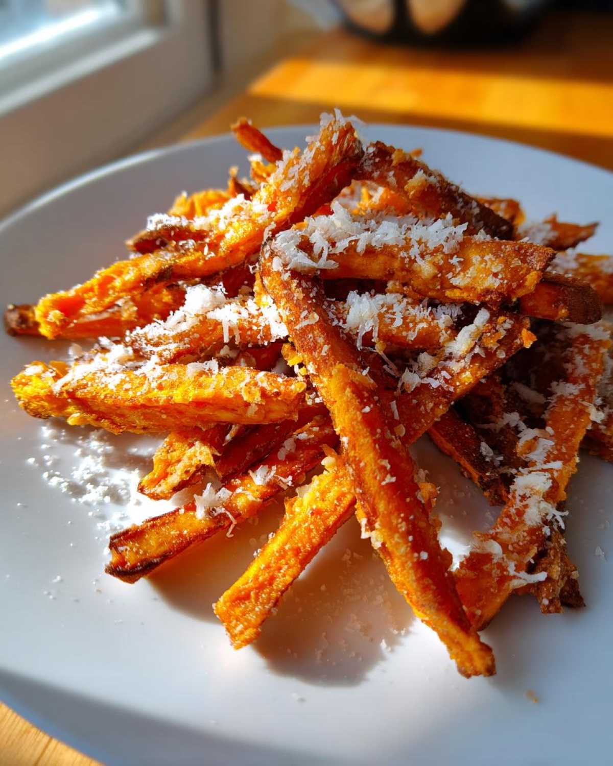 A pile of crispy Air Fryer Garlic Parmesan Sweet Potato Fries topped with grated white cheese.