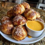 A pile of golden brown Air Fryer Pretzel Bites sprinkled with coarse salt next to a small bowl of bright yellow beer cheese dip.