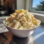 A white bowl filled high with creamy Copycat Deli-Style Macaroni Salad featuring elbow macaroni, celery, and specks of carrot.