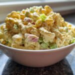 A white bowl filled high with creamy Copycat Deli-Style Macaroni Salad featuring elbow macaroni, celery, and red onion.