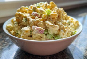 A white bowl filled high with creamy Copycat Deli-Style Macaroni Salad featuring elbow macaroni, celery, and red onion.