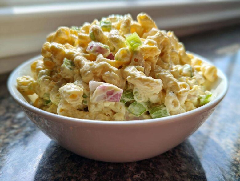 A white bowl filled high with creamy Copycat Deli-Style Macaroni Salad featuring elbow macaroni, celery, and red onion.