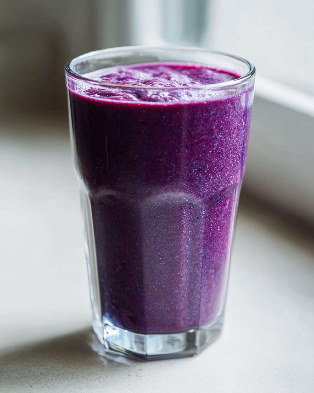 A tall glass filled with a thick, vibrant purple Creamy Blueberry Banana Smoothie.