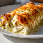 Close-up of Creamy White Chicken Enchiladas smothered in melted, bubbly cheese and green chile sauce.