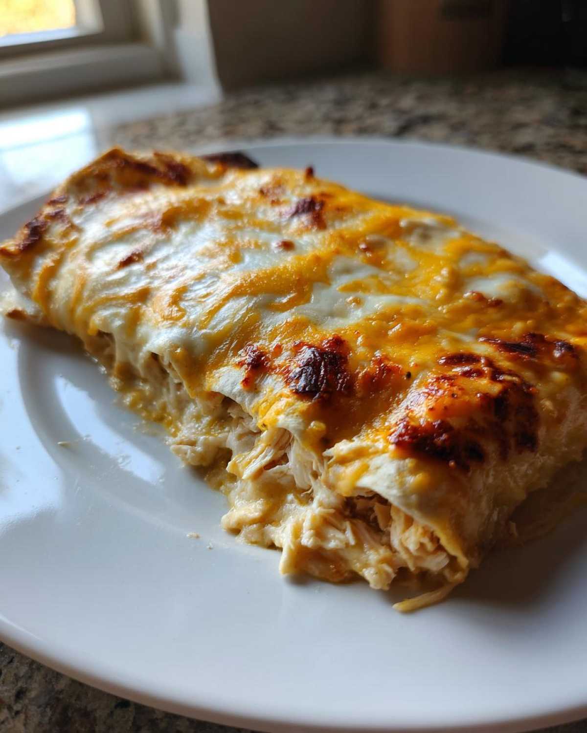 A serving of Creamy White Chicken Enchiladas showing shredded chicken filling under melted white and orange cheese.