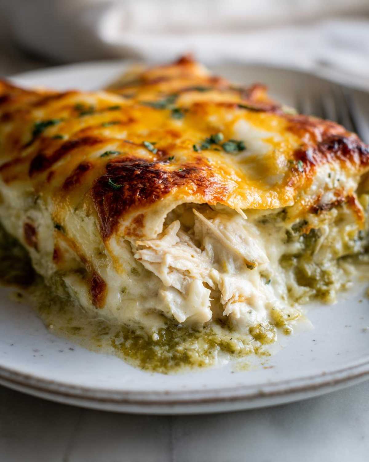 Close-up of Creamy White Chicken Enchiladas showing shredded chicken filling and green chile sauce.