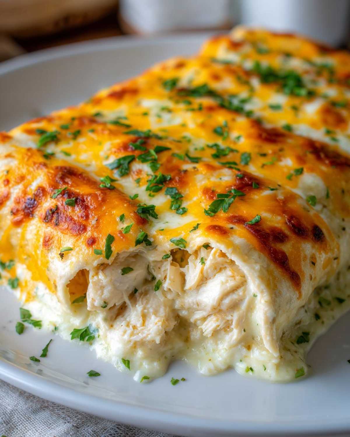 Close-up showing the shredded chicken filling oozing out of a baked Creamy White Chicken Enchilada topped with melted cheese.