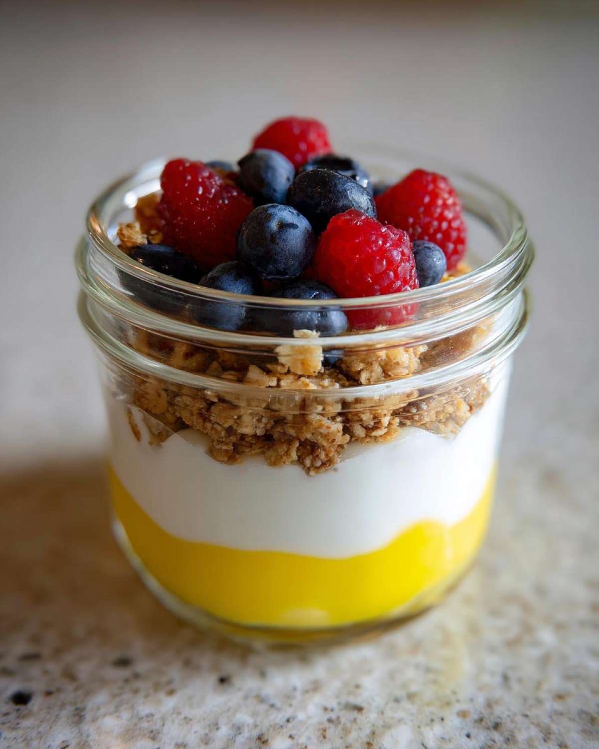 Close-up of an Easy Lemon Poppy Seed Yogurt Parfait layered with lemon curd, yogurt, granola, blueberries, and raspberries.