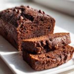 A rich, dark loaf of Gluten-Free Chocolate Zucchini Bread, partially sliced, topped with melted chocolate chips.