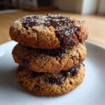 A stack of three chewy Gluten-Free Irish Oat Cookies with melted dark chocolate chunks and coarse sugar sprinkled on top.