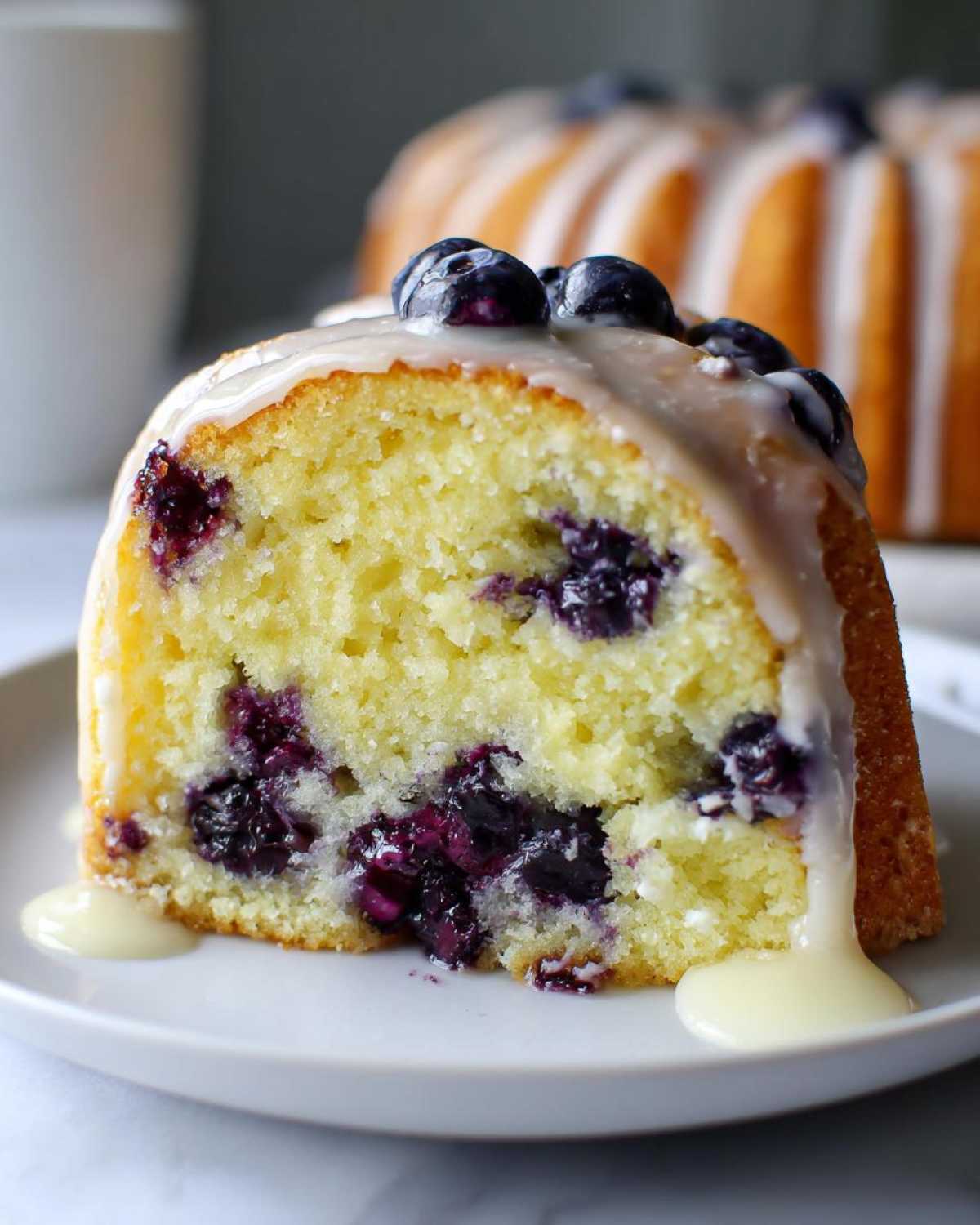 Close-up of a moist slice of Gluten-Free Lemon Blueberry Bundt Cake topped with lemon glaze and fresh blueberries.