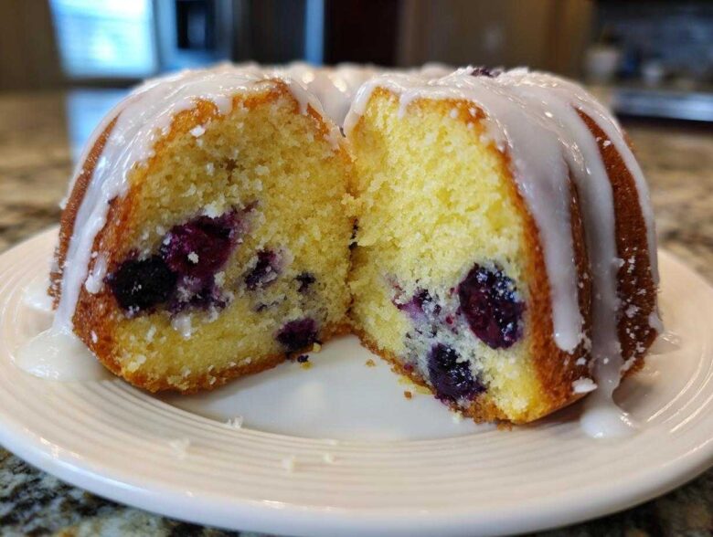 Cross section of a moist Gluten-Free Lemon Blueberry Bundt Cake showing blueberries inside and a lemon glaze on top.