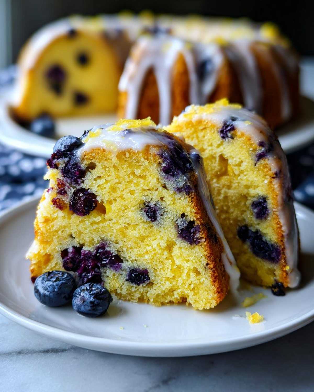 Two slices of moist Gluten-Free Lemon Blueberry Bundt Cake topped with lemon glaze and fresh blueberries.