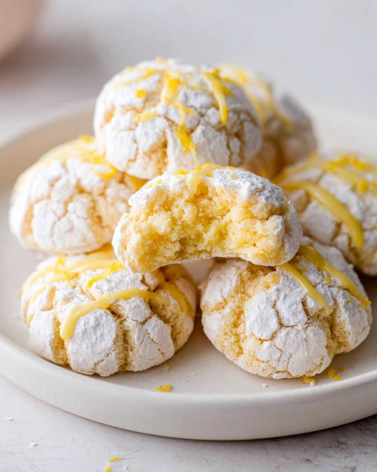 A stack of Gluten-Free Lemon Meltaway Cookies dusted with powdered sugar, one is broken open showing the soft interior.