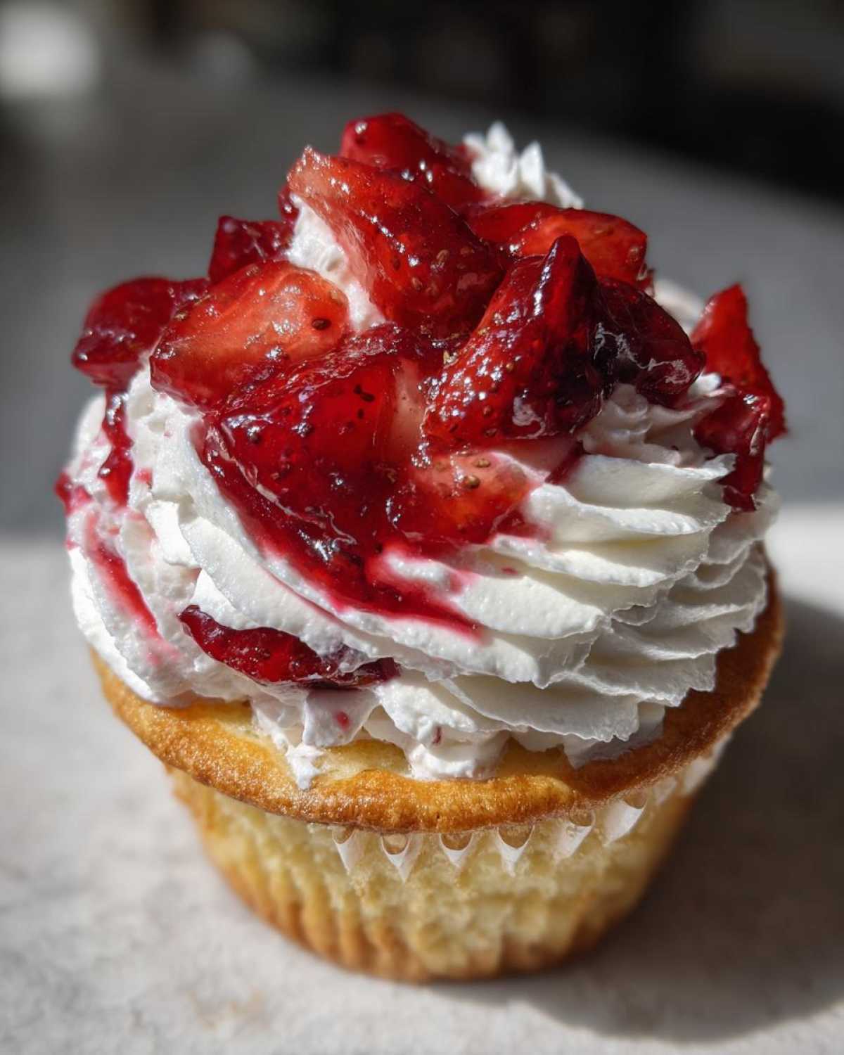 A close-up of a moist Gluten-Free Strawberry Shortcake Cupcake topped with whipped cream and macerated strawberries.