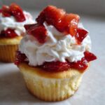 A close-up of a Gluten-Free Strawberry Shortcake Cupcakes topped with whipped cream and macerated strawberries.