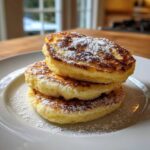A stack of three fluffy High-Protein Cottage Cheese Pancakes dusted with powdered sugar.