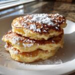 A stack of three fluffy High-Protein Cottage Cheese Pancakes dusted generously with powdered sugar.