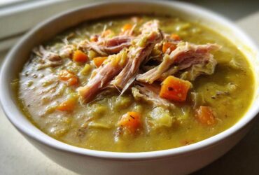 A close-up of a white bowl filled with thick Instant Pot Split Pea Soup with Smoked Turkey and diced carrots.